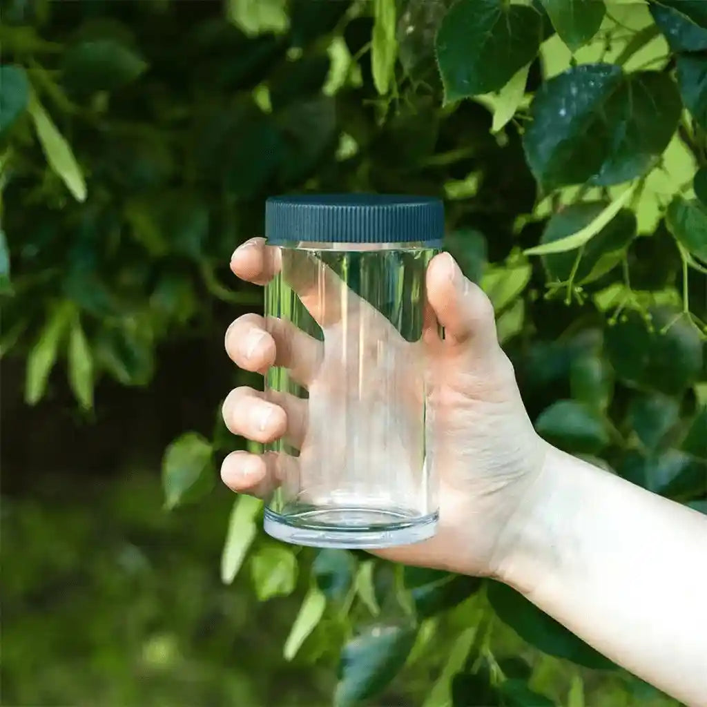 Ersatzbehälter transparent in der Hand, im Hintergrund grünes Gebüsch
