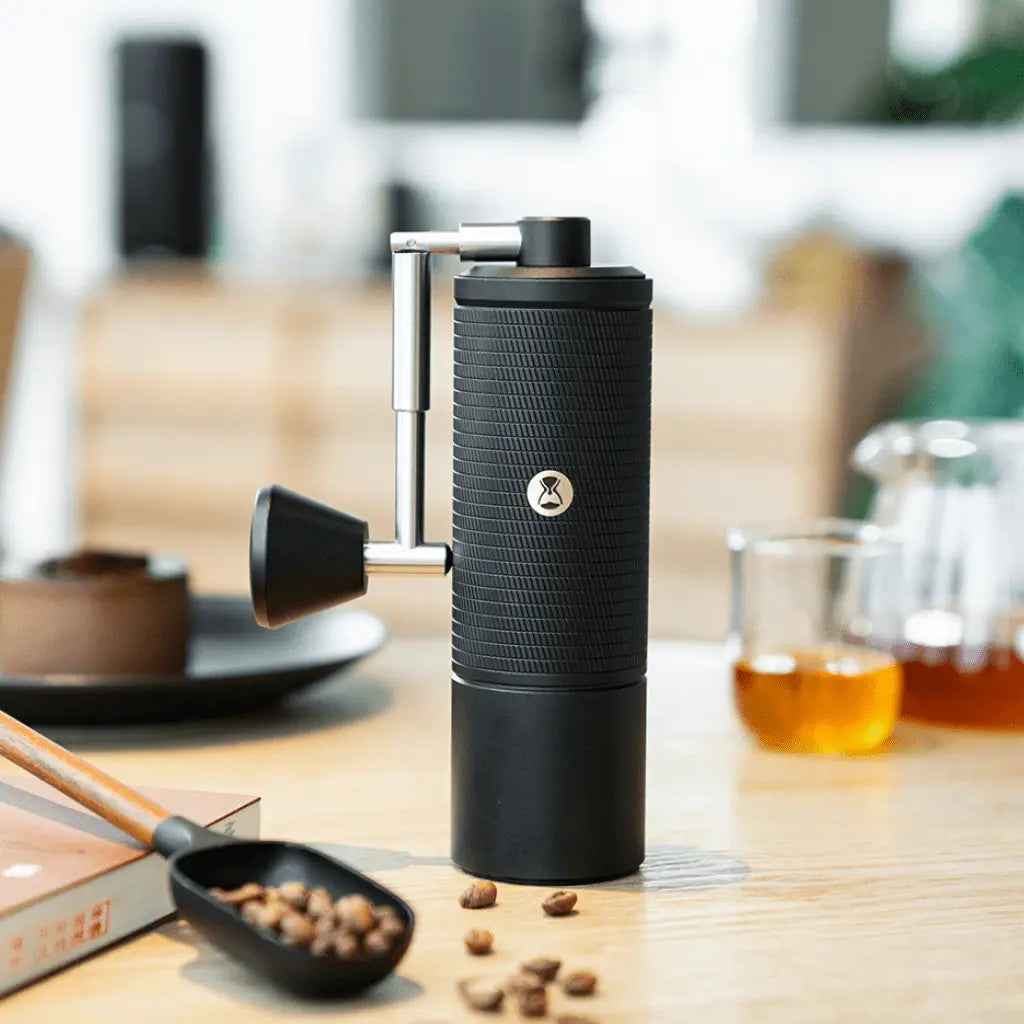 Timemore C5 ESP Pro Handkaffeemühle aus schwarzem Aluminium auf einem Holztisch, mit Kaffeebohnen und Zubehör im Hintergrund.